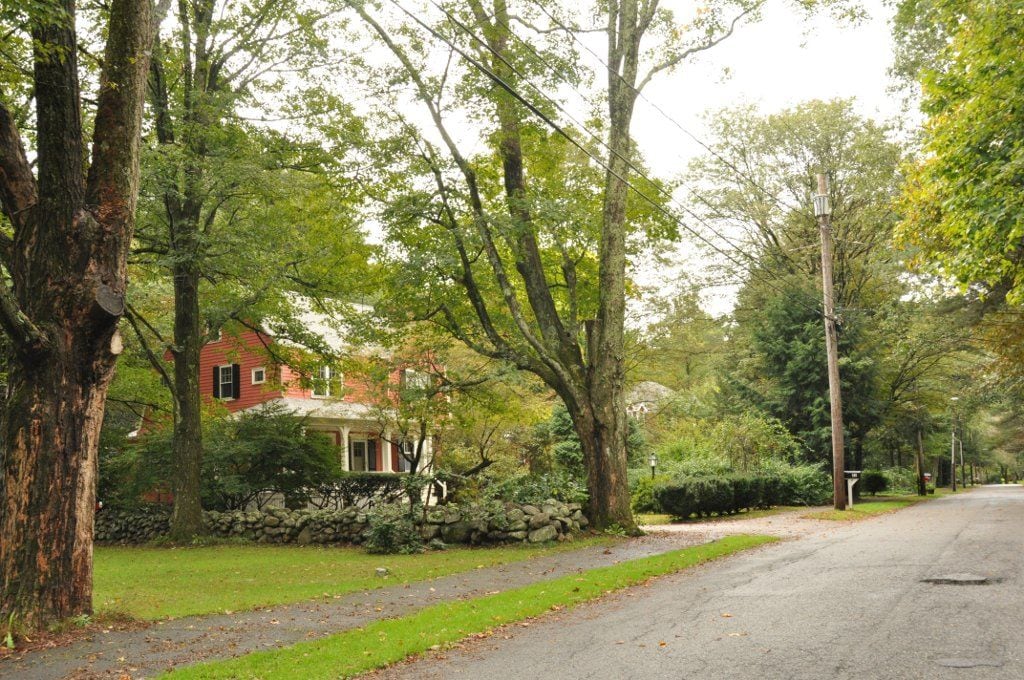 Tree-lined Silver Hill Road with a red home and stone wall in Weston, Massachusetts